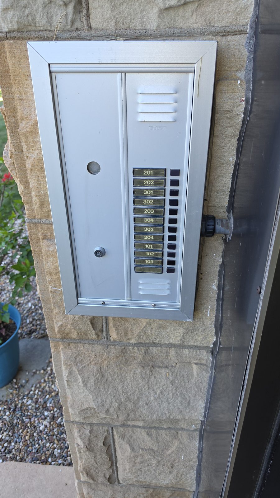 The building entry panel: a TekTone intercom with tenant call buttons, wiring conduit exposed at right.